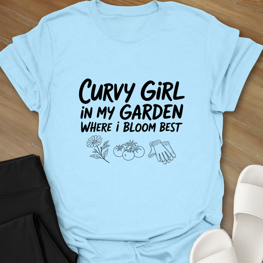 Light blue Curvy girl gardening shirt with white hand-lettered text reading “Curvy Girl in My Garden Where I Bloom Best” and garden icons on black background